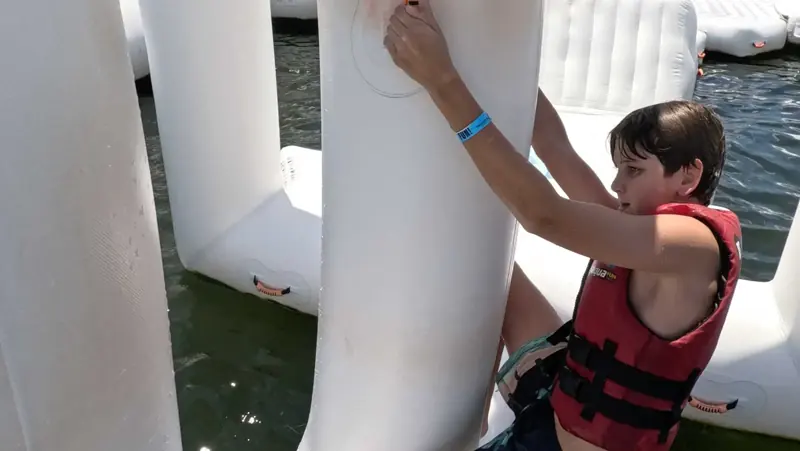 Young Aqua Warrior gripping a vertical inflatable obstacle