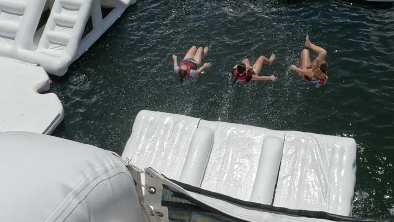 Three guests jumping into the water beside an obstacle